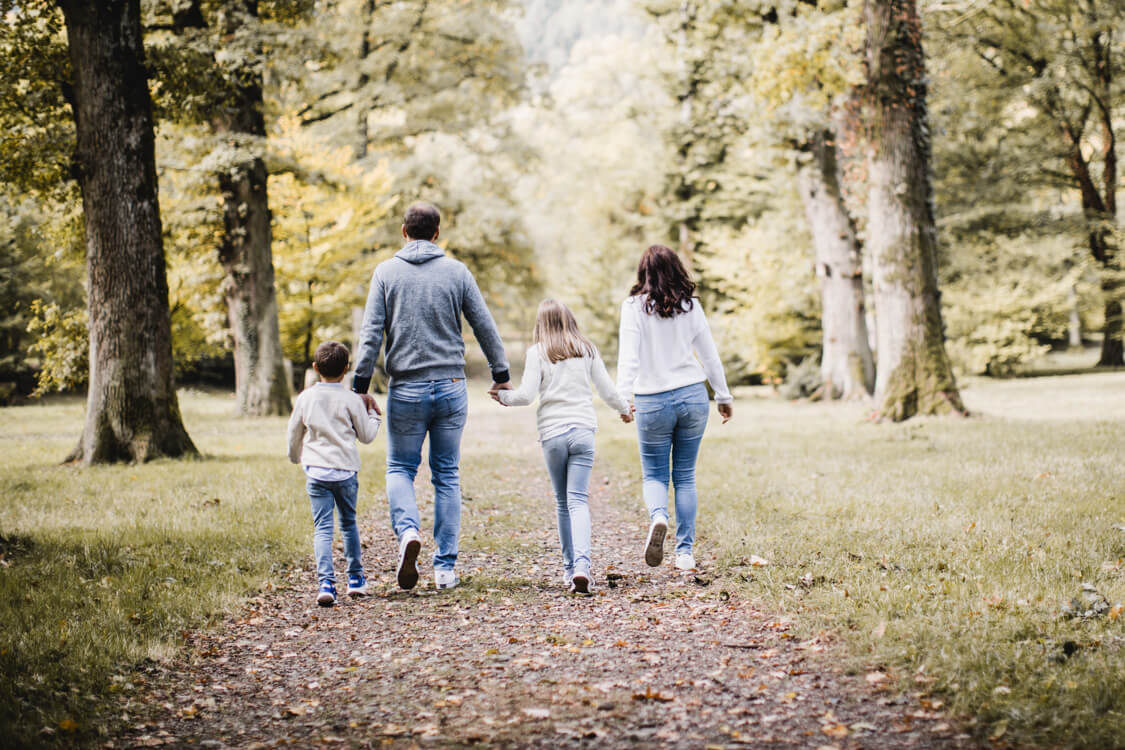 Familie hält sich an den Händen und ist von hinten zu sehen