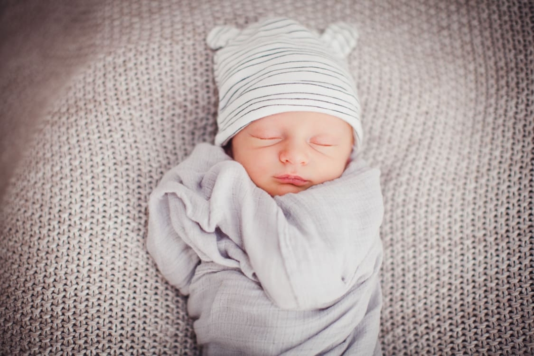 Baby mit Mütze liegt eingepuckt auf einer Decke