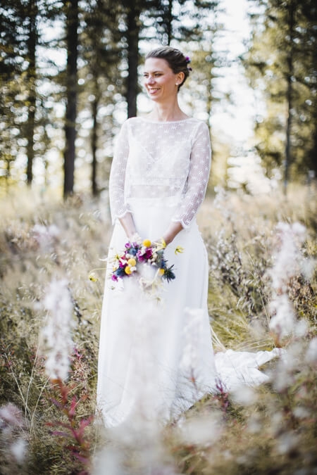 Braut steht auf einer Blumenwiese am Waldrand