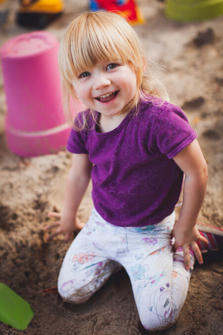 Mädchen sitzt im Sandkasten und lacht