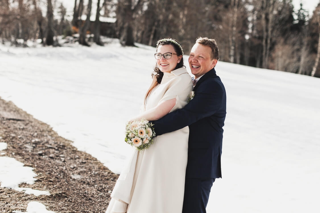 Bräutigam umarmt Braut von hinten vor Schneekulisse