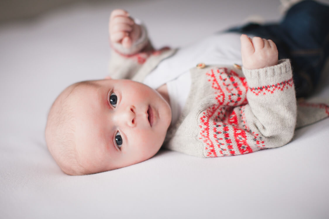 Baby mit Strickjacke liegt auf Bett