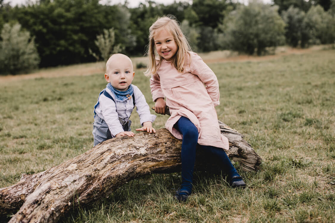 Mädchen mit kleinem Bruder auf einem Baumstamm