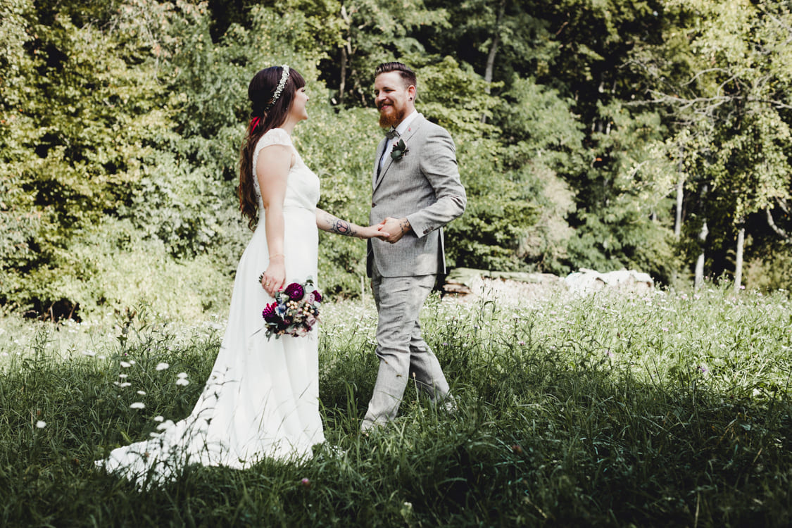 Brautpaar auf eiiner Wiese. Der Bräutigam streckt nach der Braut die Hand aus die ihm gegenüber steht.