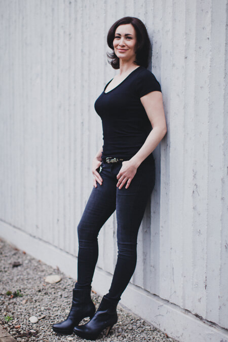 Frau mit schwarzer Hose und schwarzem T-Shirt lehnt an einer Wand