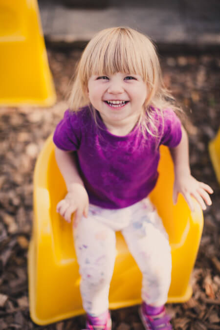 Mädchen sitzt auf einem gelben Stuhl und lacht