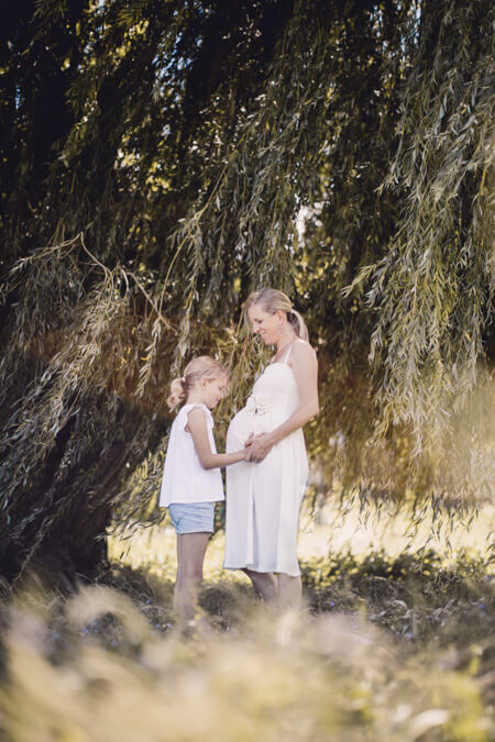 Mädchen steht ihrer Mutter gegenüber und hält die Hände auf ihren Babybauch