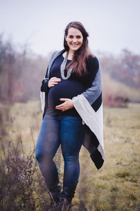Schwangere Frau mit Strickmantel hält ihren Babybauch