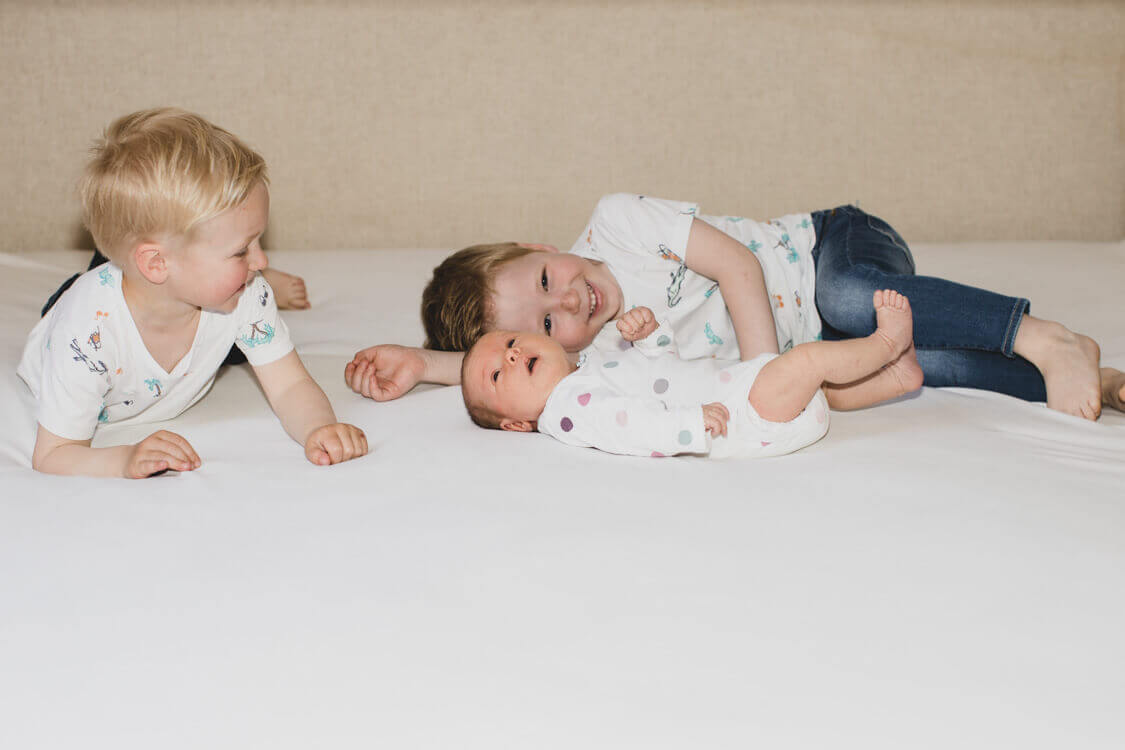 Brüder kuscheln mit ihrer kleinen Schwester auf einem Bett