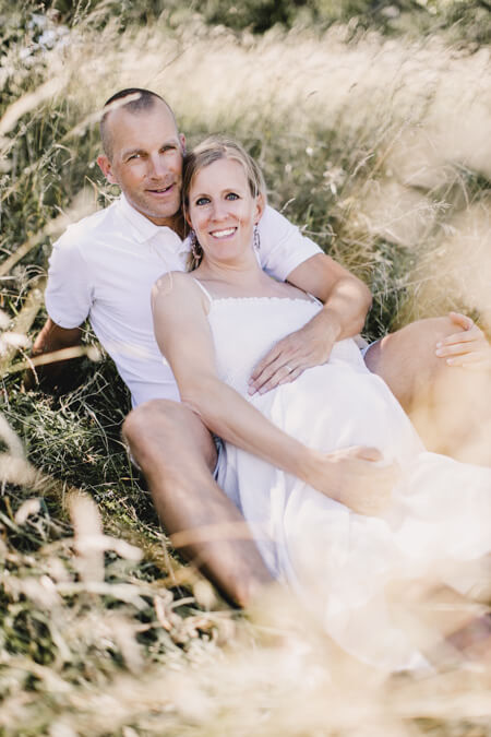 Paar sitzt auf einer Wiese. Die Frau hat einen Babybauch.