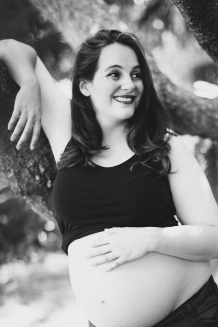 Frau mit Babybauch lehnt an Baum