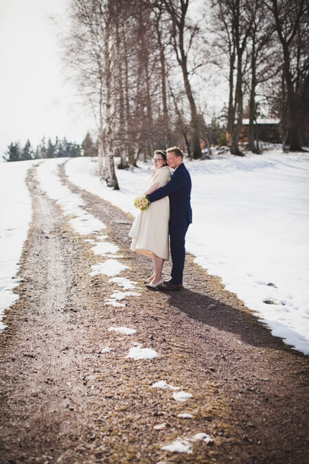 Bräutigam umarmt Braut von hinten auf einem Weg inmitten einer Schneekulisse