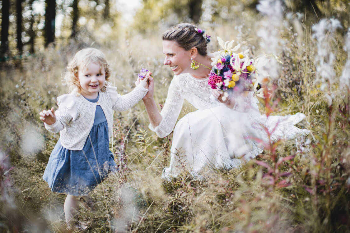 Braut sitzt in der Hocke und hält ihre Tochter an der Hand