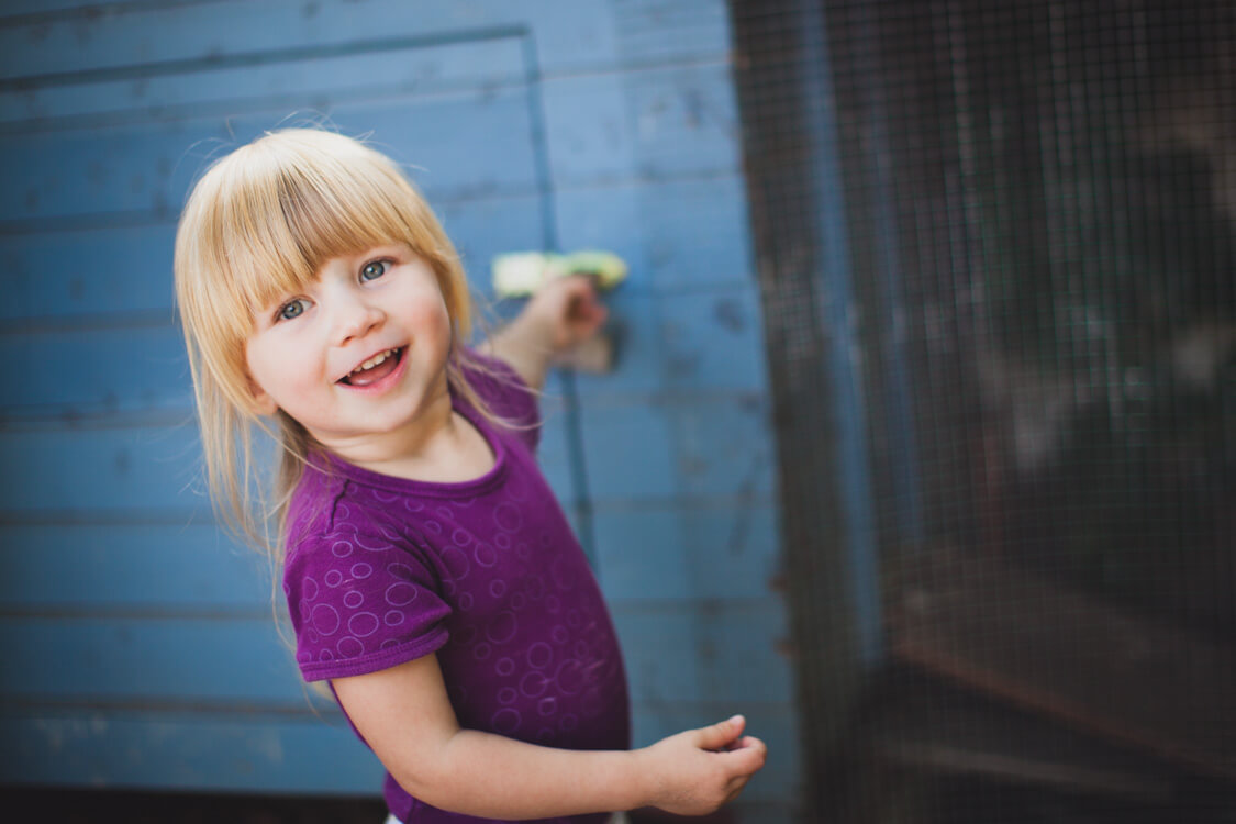 Mädchen steht vor blauem Holzschuppen