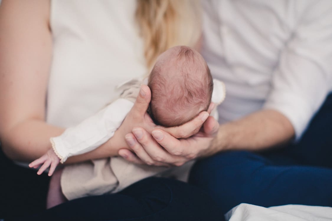 Nahaufnahme von Eltern die ihr Neugeborenes gemeinsam im Arm halten