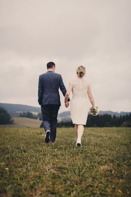Brautpaar von hinten zusehen wie sie über eine Wiese laufen