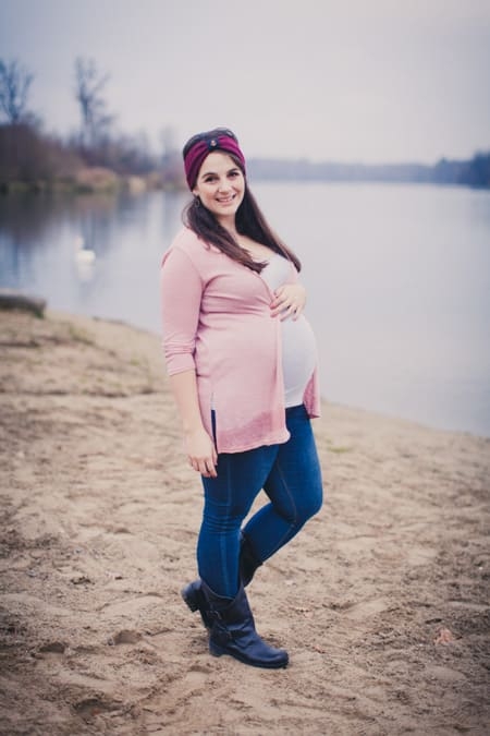 Schwangere Frau mit rosa Strickjacke steht am See