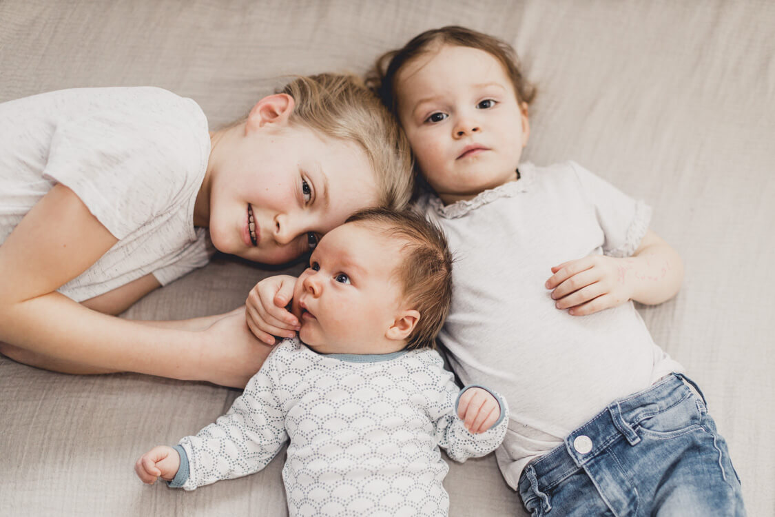 Drei Geschwister liegen eng mit ihren Köpfen beieinander