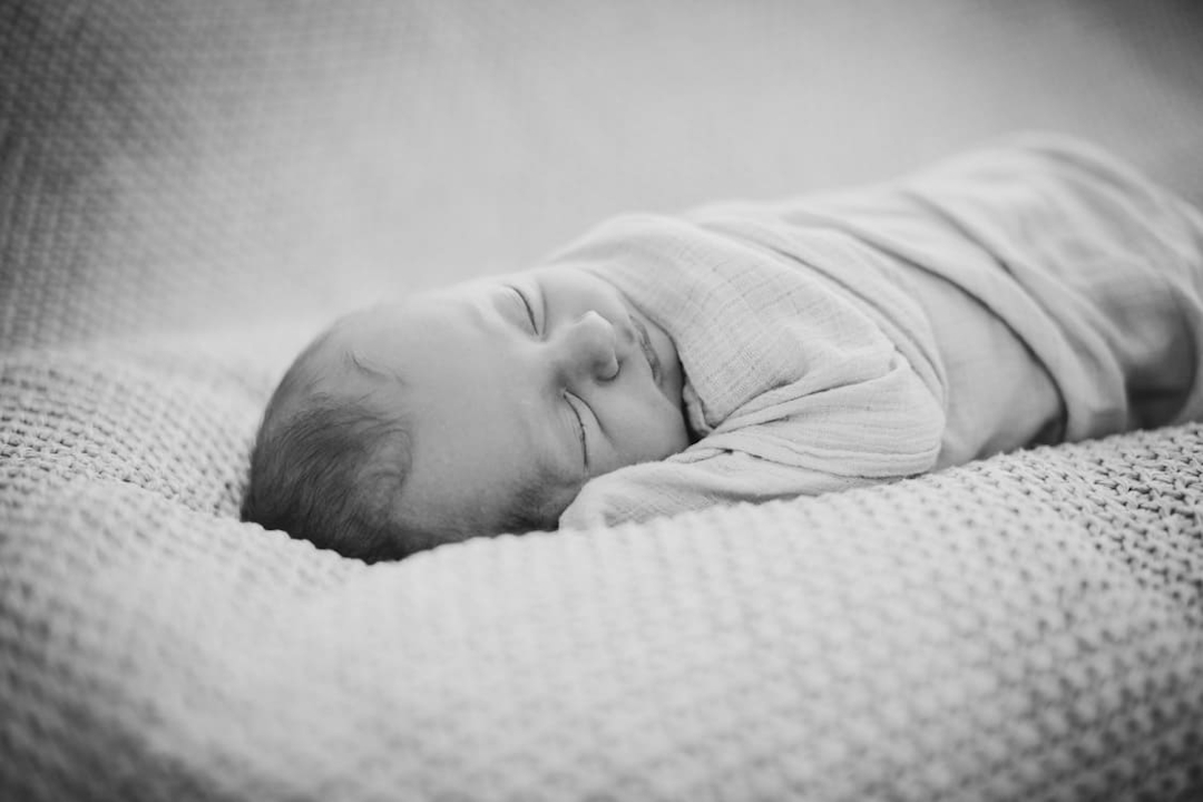 Schwarz Weiß Aufnahme von schlafendem Baby in einer Decke eingepuckt
