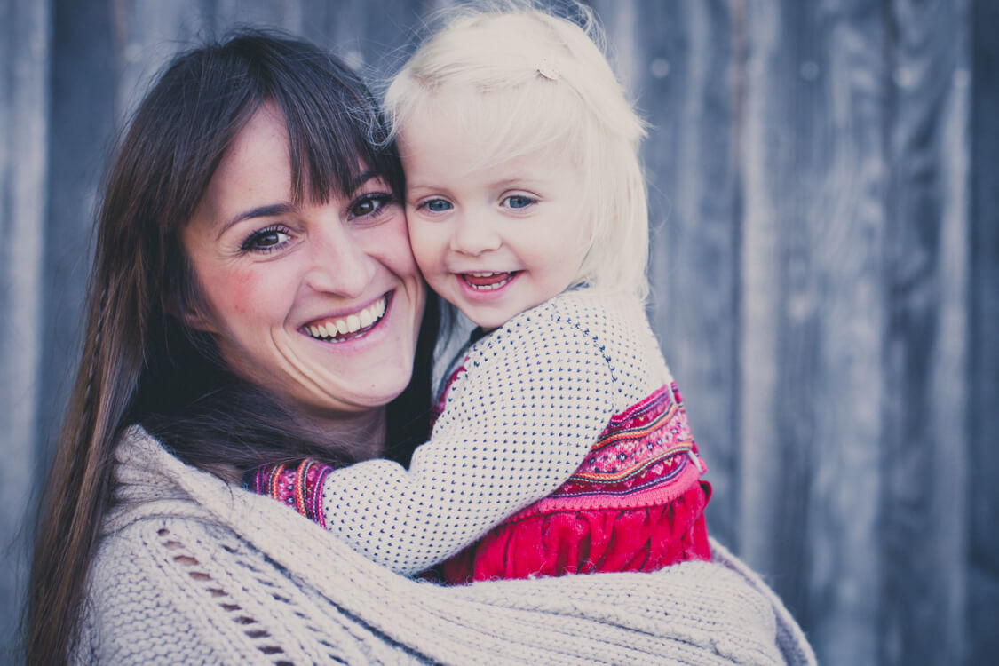 Mutter hat ihre Tocher auf dem Arm in ihrem Strickmantel eingewickelt