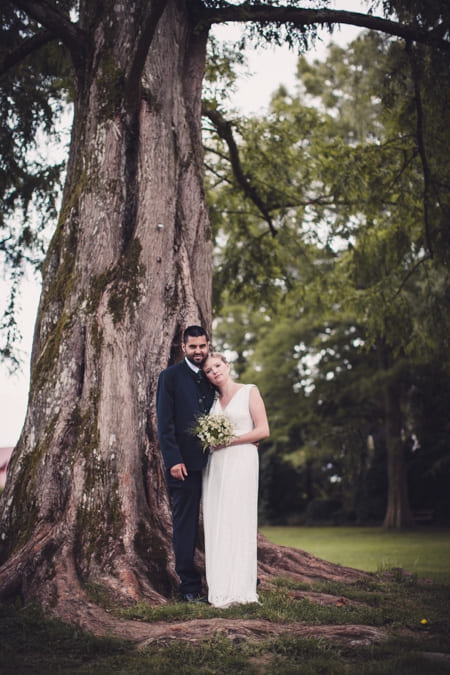 Braut lehnt sich an ihrem Bräutigam an. Sie stehen unter einem Baum.