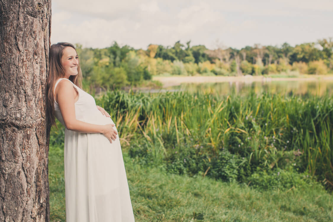 Frau lehnt am Baum mit Babybauch