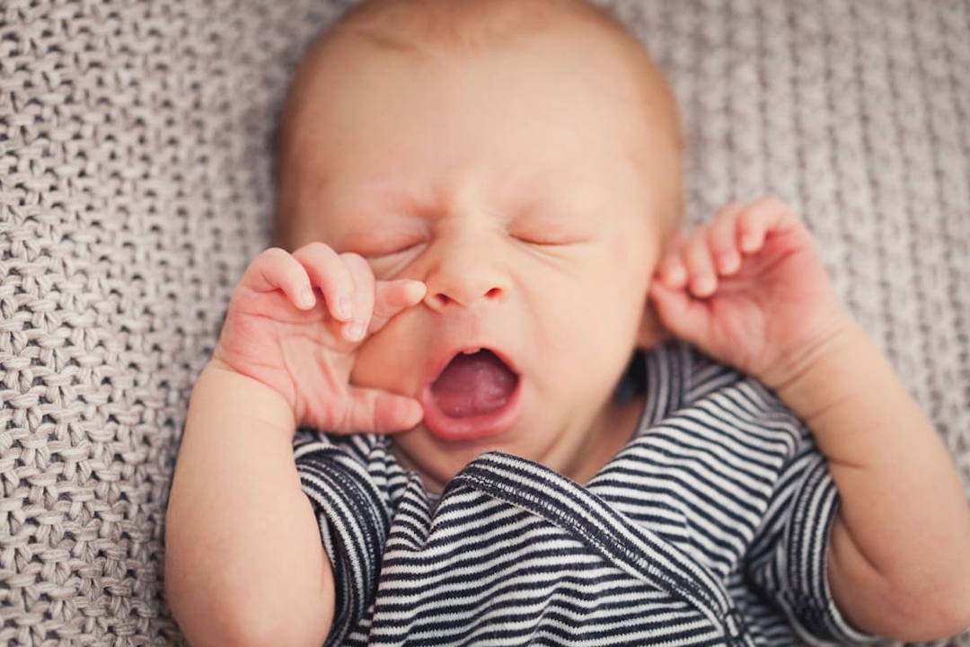 Gähnenendes Baby auf einer gestrickten Decke