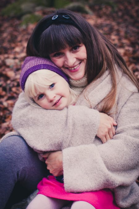 Mama kuschelt mit ihrer Tochter und nimmt sie unter ihren Strickmantel