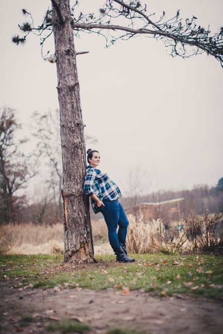 Schwangere Frau mit Karohemd lehnt an einem Baum