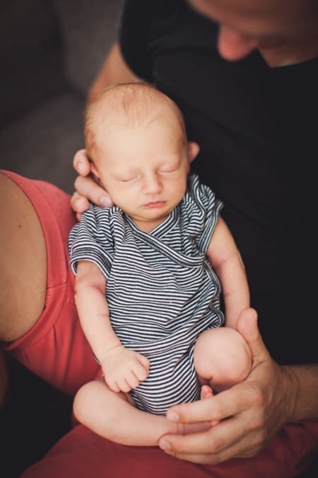 Vater hält seinen schlafenden Neugeborenen Sohn auf dem Schoß