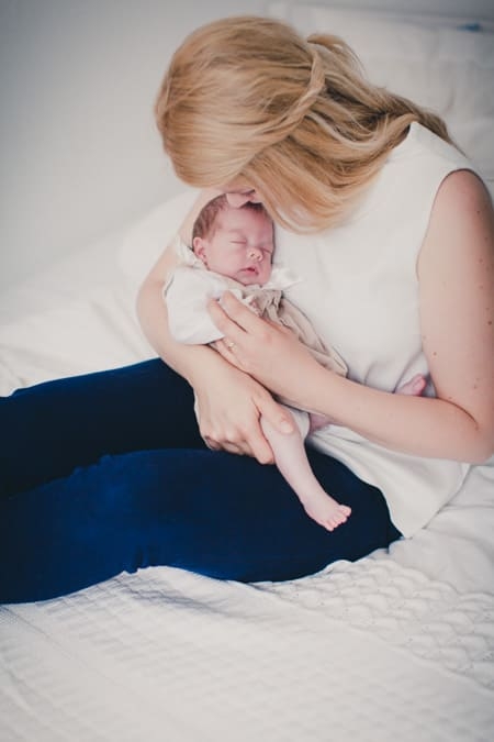 Mutter sitzt miot Neugeborenen im Arm auf dem Bett