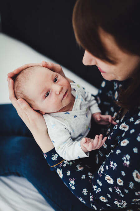 Baby liegt auf dem Schoß seiner Mutter die den Kopf mit iheren Händen umschließt