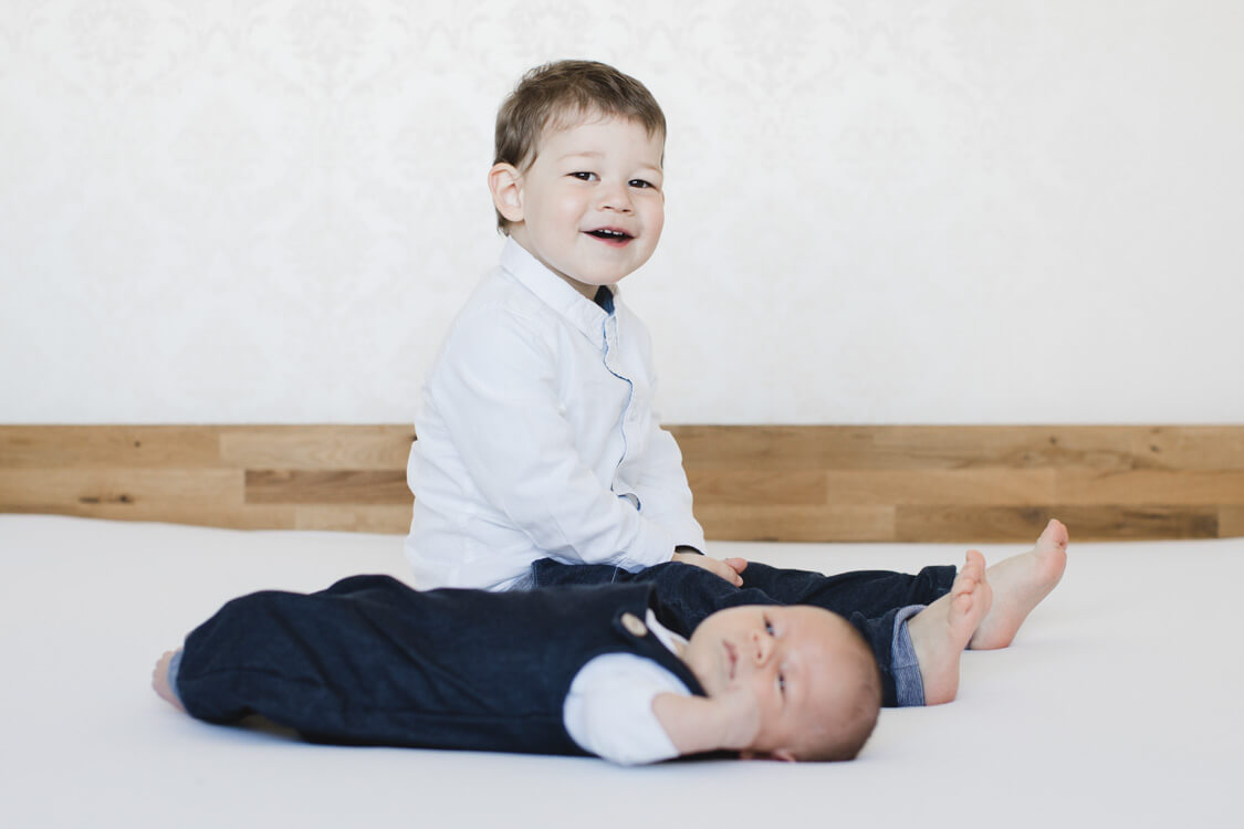 Junge sitzt auf dem Bett. Vor ihm liegt sein Bruder.