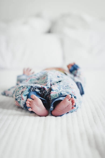 Neugeborenes liegt auf dem Bett und steckt die Füße in die Kamera