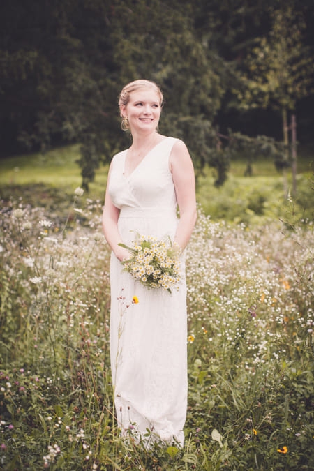 Braut in Blumenwiese und Brautstrauß in der Hand