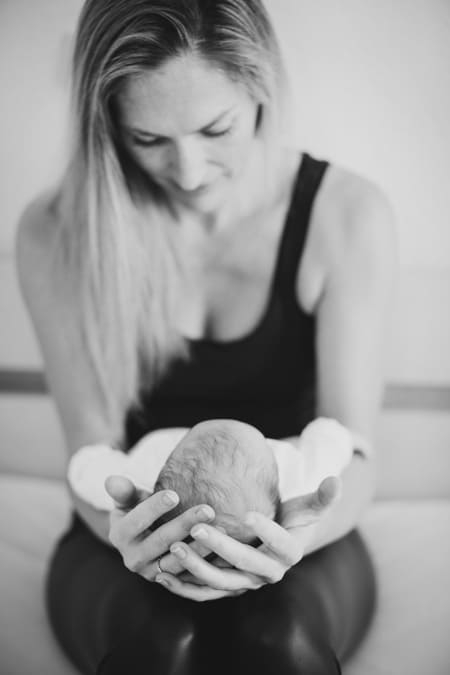 Frau hält Köpfchen vom Baby in den Händen. Schwarz-weiß Fotografie.