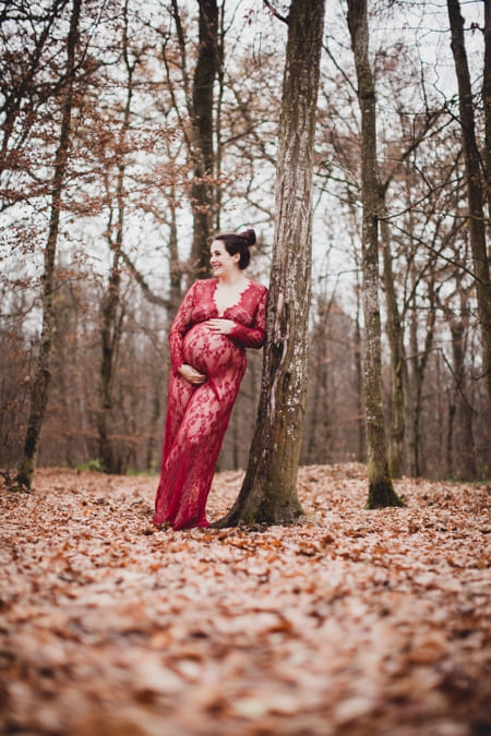 Schwangere Frau im roten Spitzenkleid im Herbstwald