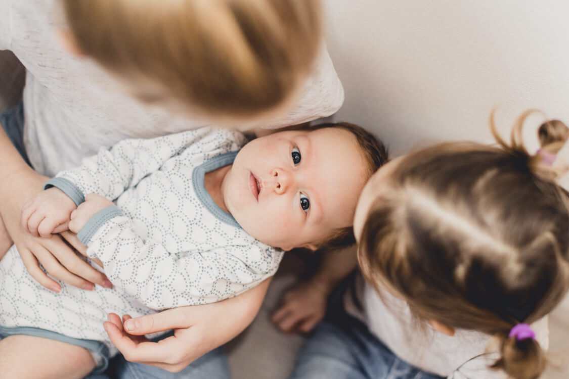 Schwestern halten ihren kleinen Bruder auf dem Schoß. Blick von oben auf das Baby.