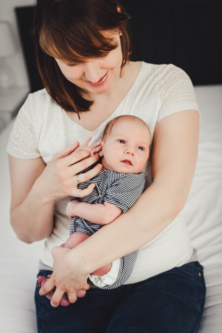 Mutter sitzt auf der kante vom Bett und hält ihr Baby im Arm