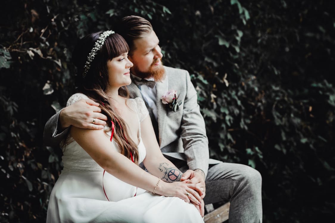 Brautpaar sitzt auf der Lehne einer Bank und blickt in die Ferne