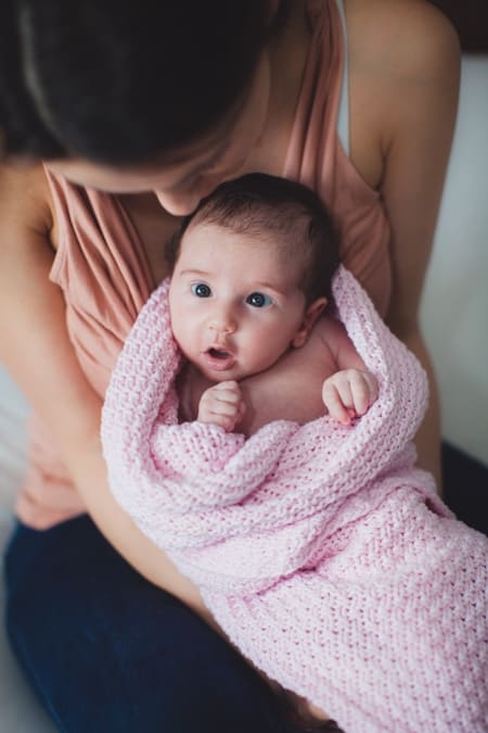 Baby in Decke eingewickelt sitzt bei Mama auf dem Schoß