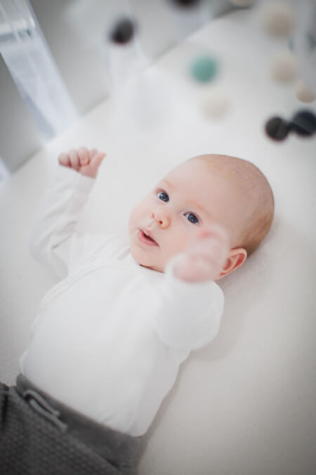 Baby liegt in seinem Bett. Darüber hängt ein Mobile.