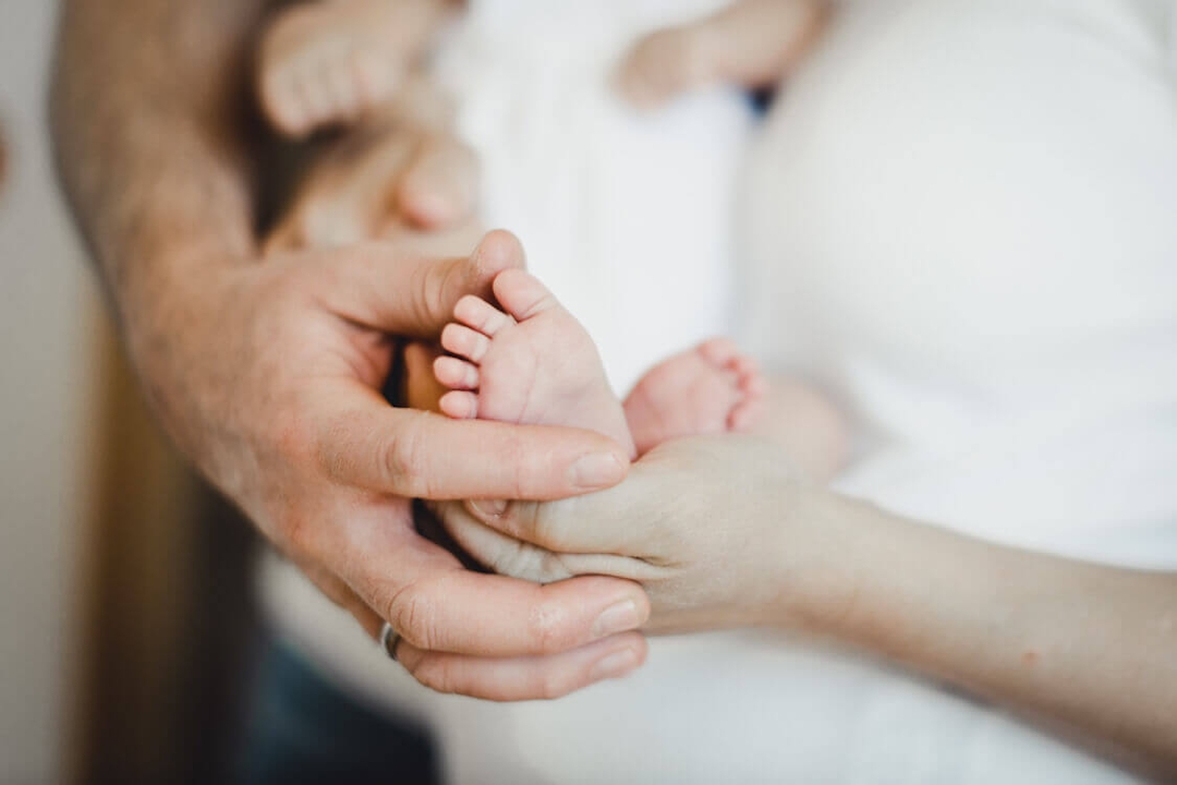 Eltern halten die Füße ihres Babys zusammen in ihren Händen