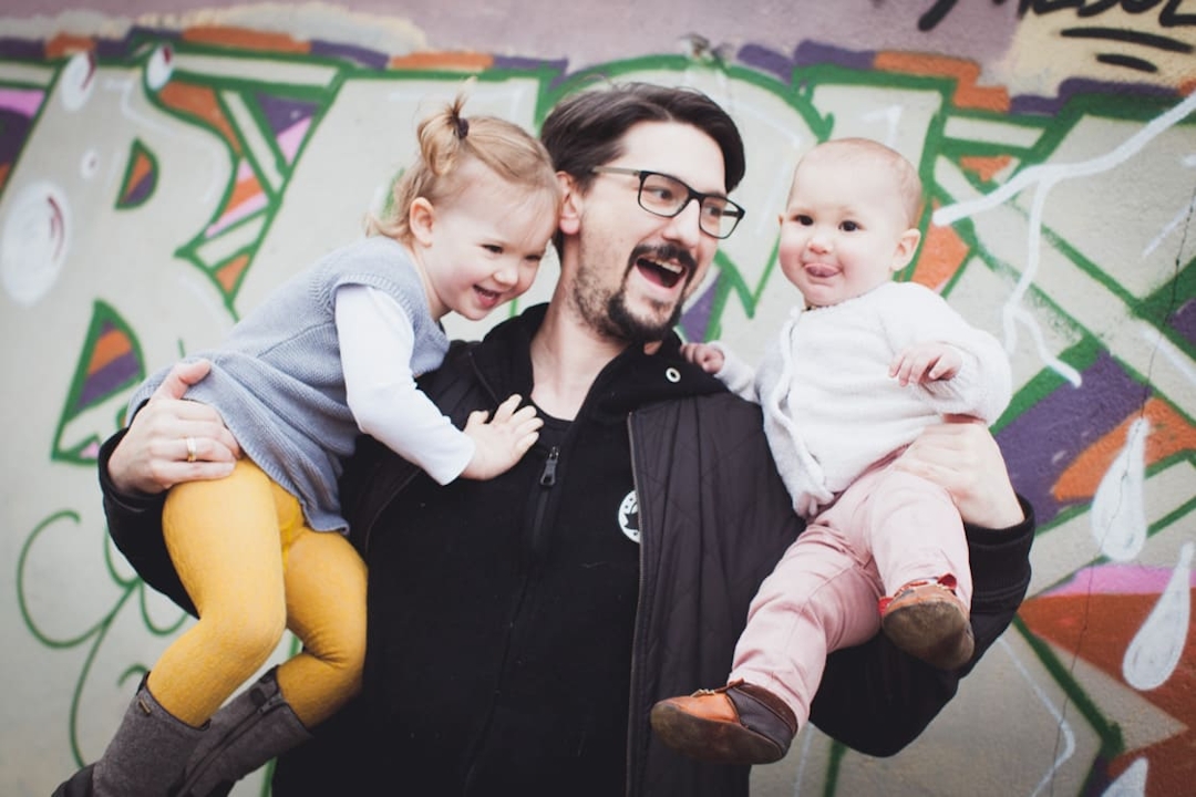 Papa mit seinen beiden Töchtern auf dem Arm vor einem Grafiti