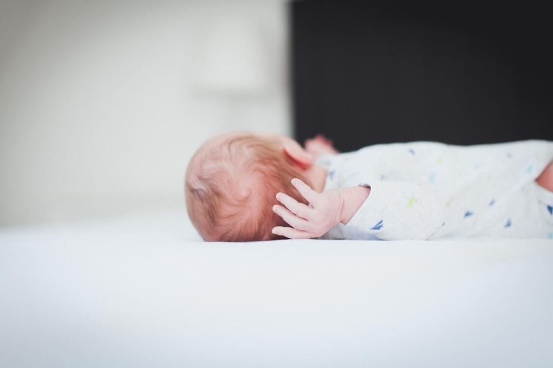 Hinterkopf und Hand von einem Neugeborenen Baby das auf einem Bett liegt