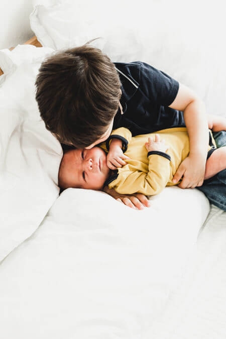 Junge kuschelt seinenen Neugeborenen Bruder auf dem Bett