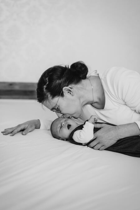 Baby liegt auf dem Bett und die Mutter beugt sich zu ihm um es zu küssen