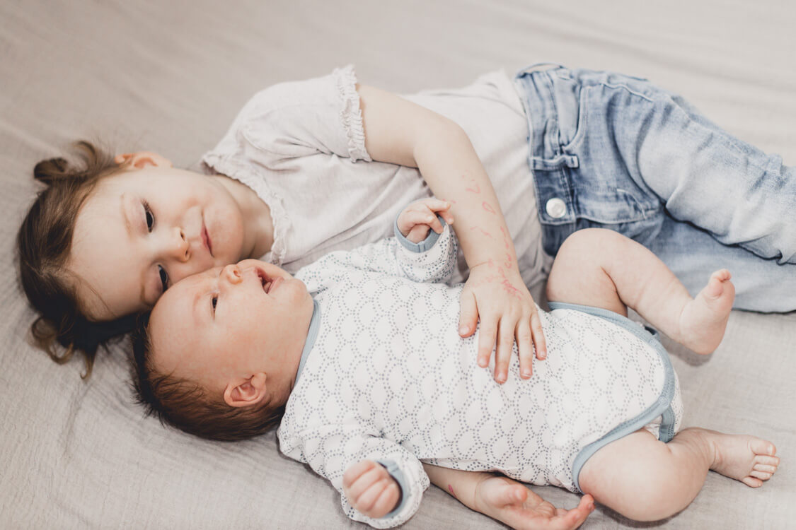 Kleine Schwester liegt mit ihrem Bruder auf dem Bett und streichelt ihn am Bauch