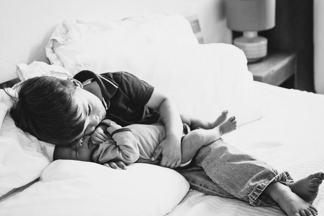 SW Foto Junge kuschelt seinenen Neugeborenen Bruder auf dem Bett