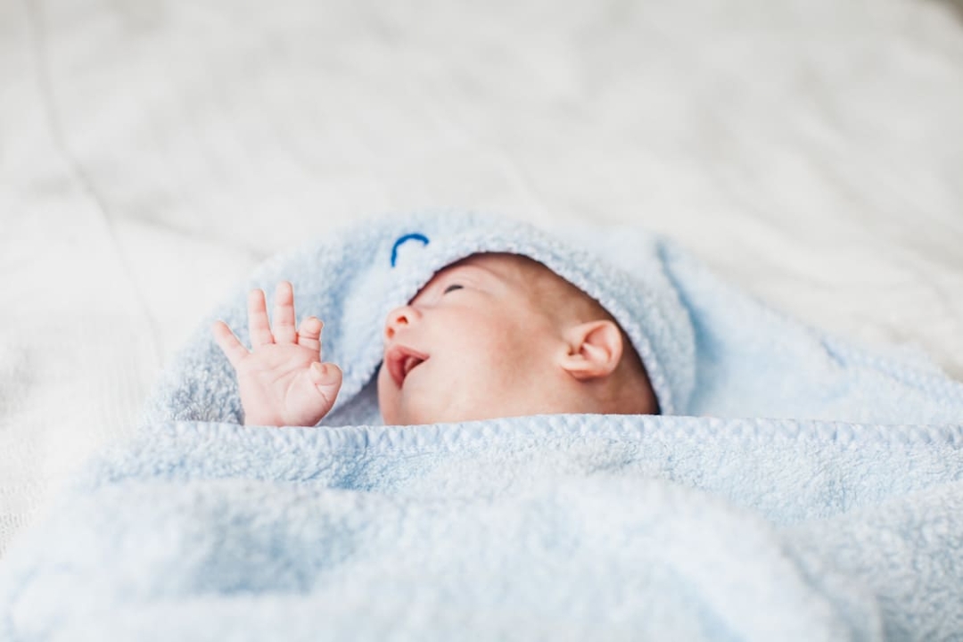 Babyhand und Kopf gucken aus blauem Handtuch hervor
